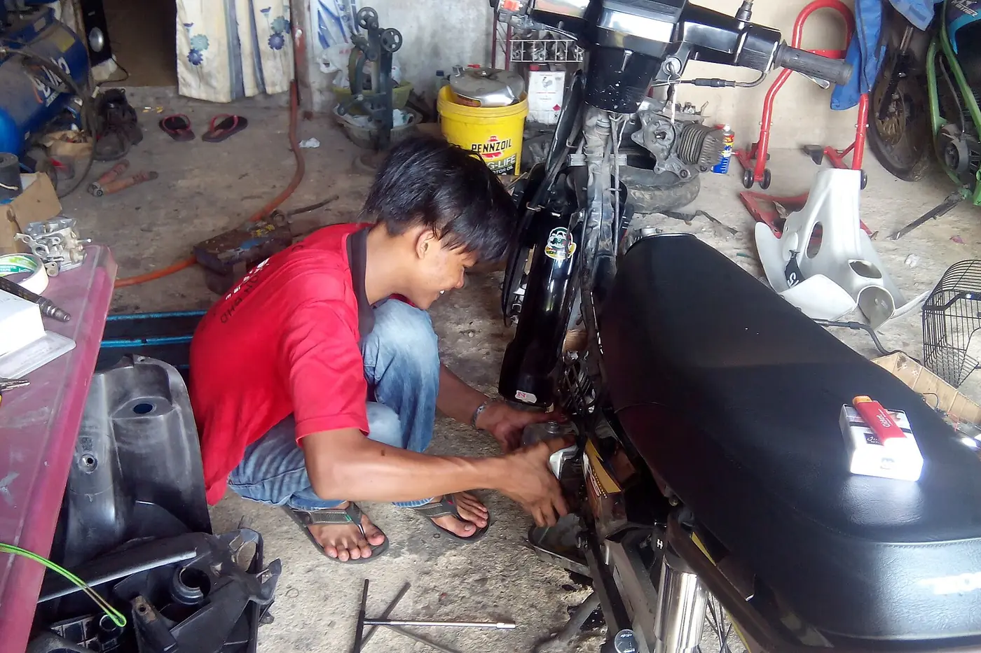 Young mechanic crouching to work on a motorcycle in a workshop