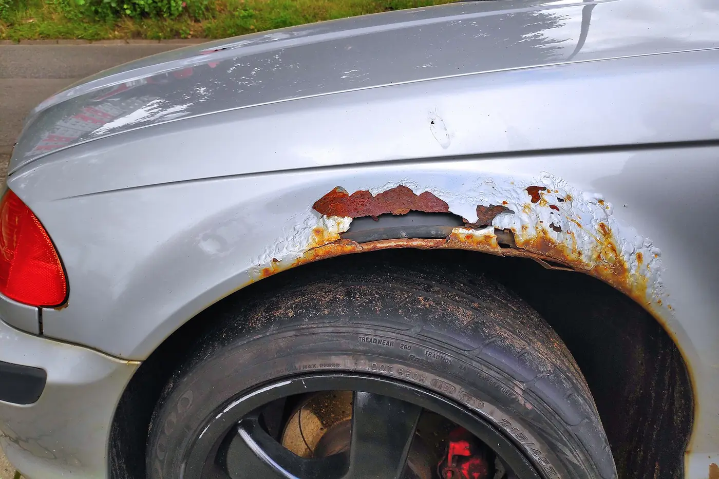 Rust bubbling through the paint above a silver car's rear wheel arch