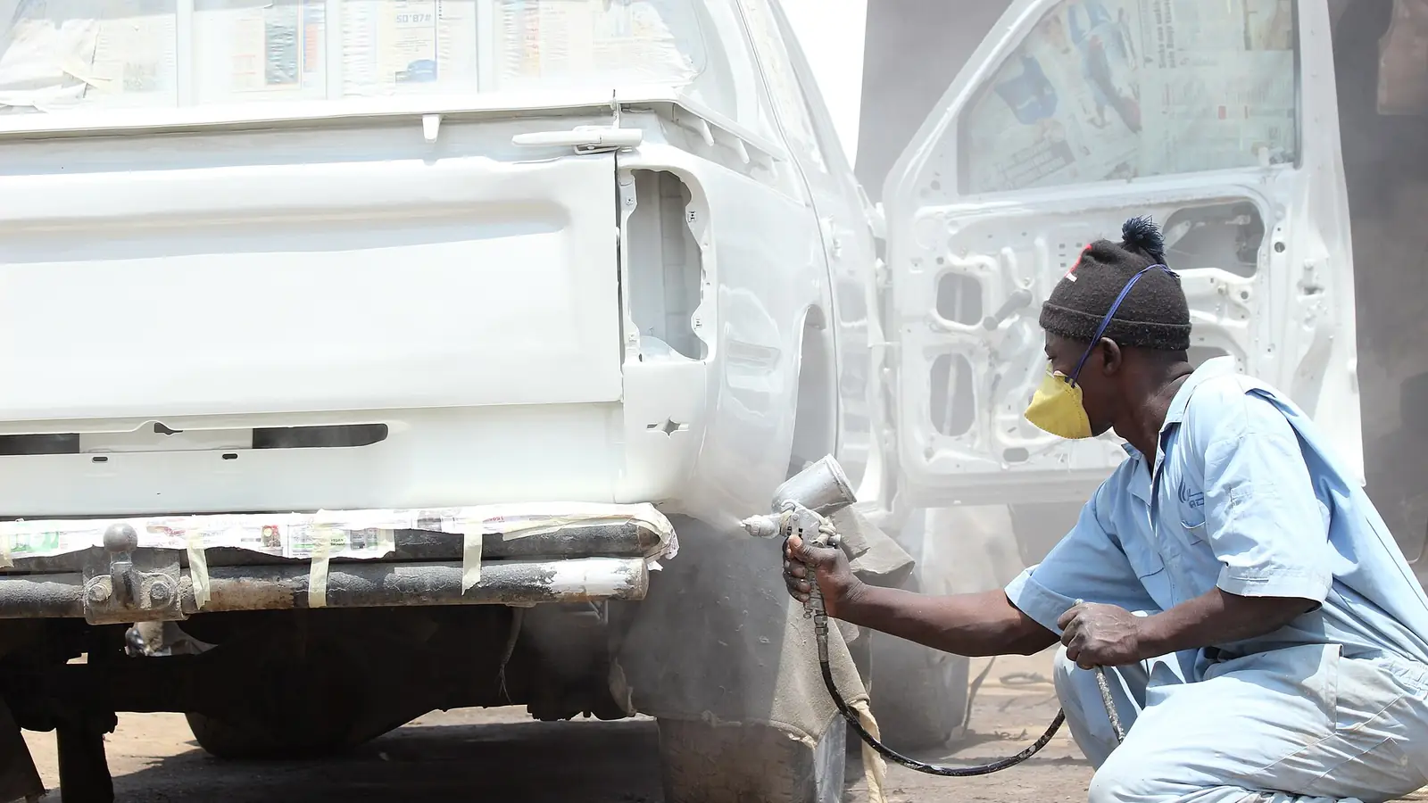 Painter in a face mask spraying the rear of a white pickup in a workshop