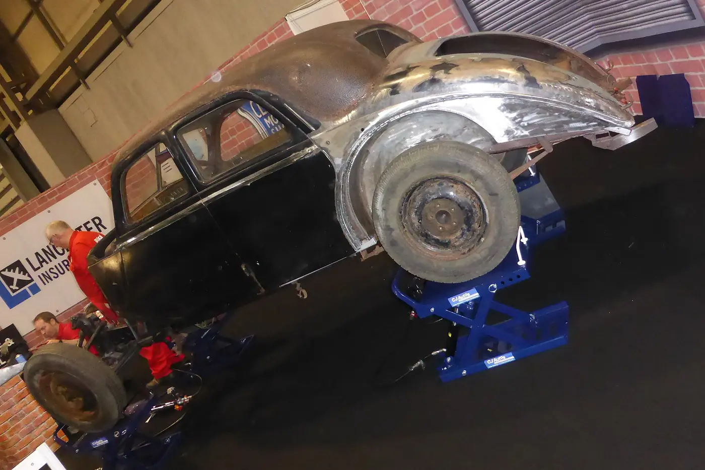 Classic car body shell on a rotisserie stand during restoration, with bare metal panels